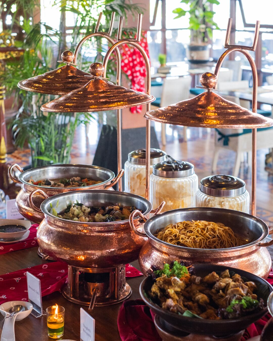 Una mesa con varios platos en ollas de cobre, una vela y un cartel con el menú.