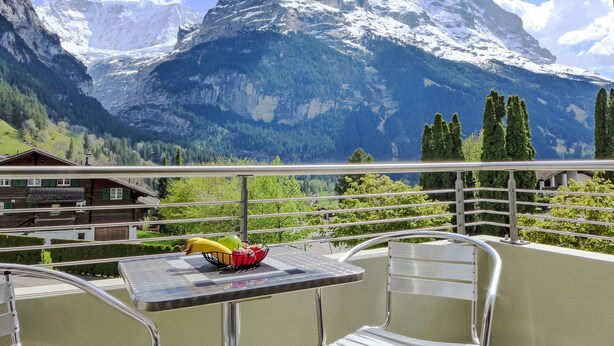 A balcony with a table and chairs, overlooking a mountain range with snow-capped peaks and a clear blue sky. - Cosy apartment for 3 people with WIFI, TV, balcony, pets allowed and panoramic view (Grindelwald)