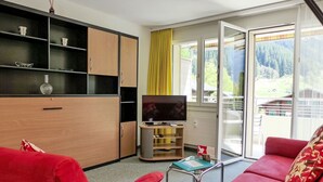 A modern living room with red sofas, a TV on a wooden stand, and a balcony with a yellow curtain. - Cosy apartment for 3 people with WIFI, TV, balcony, pets allowed and panoramic view (Grindelwald)