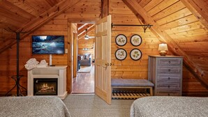 A cozy attic bedroom with a fireplace, a TV, and a view of the living area. - Heated Pool + Theater + Arcade | Near Dollywood (Sevierville)