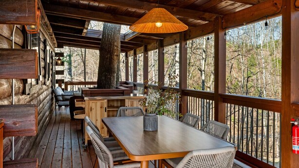 A wooden deck with a table and chairs, surrounded by wooden walls and large windows. - Heated Pool + Theater + Arcade | Near Dollywood (Sevierville)