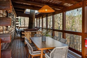 Een houten terras met een tafel en stoelen, omringd door houten wanden en grote ramen.