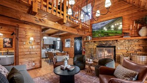 A cozy log cabin interior with a fireplace, dining area, and a living room with leather sofas and a coffee table. - Heated Pool + Theater + Arcade | Near Dollywood (Sevierville)