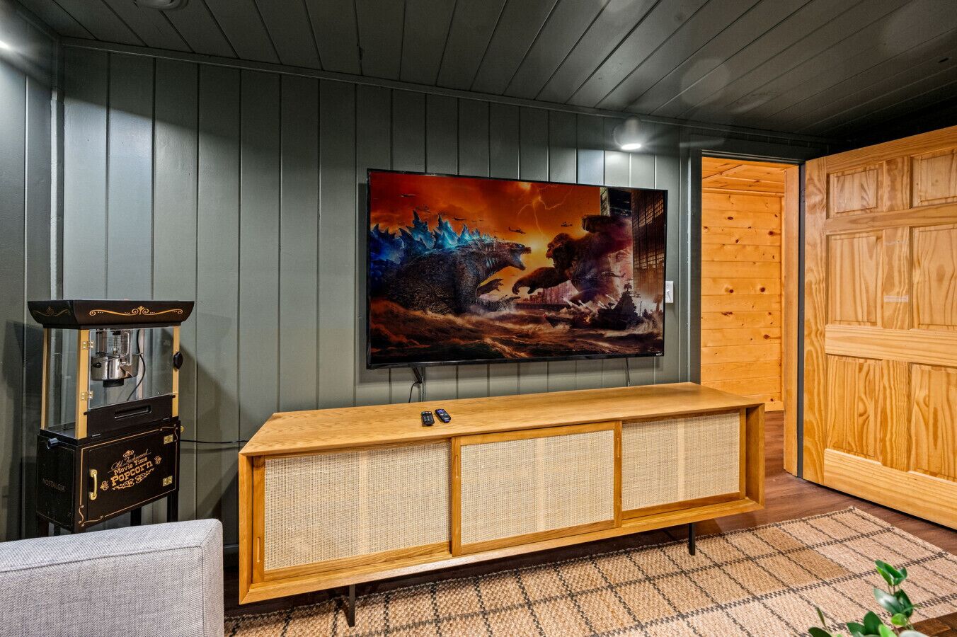 A room with a wooden entertainment center, a vintage popcorn machine, and a large framed movie poster on the wall.