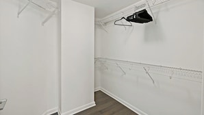 Um closet espaçoso com paredes brancas, piso de madeira e prateleiras de metal para pendurar roupas.