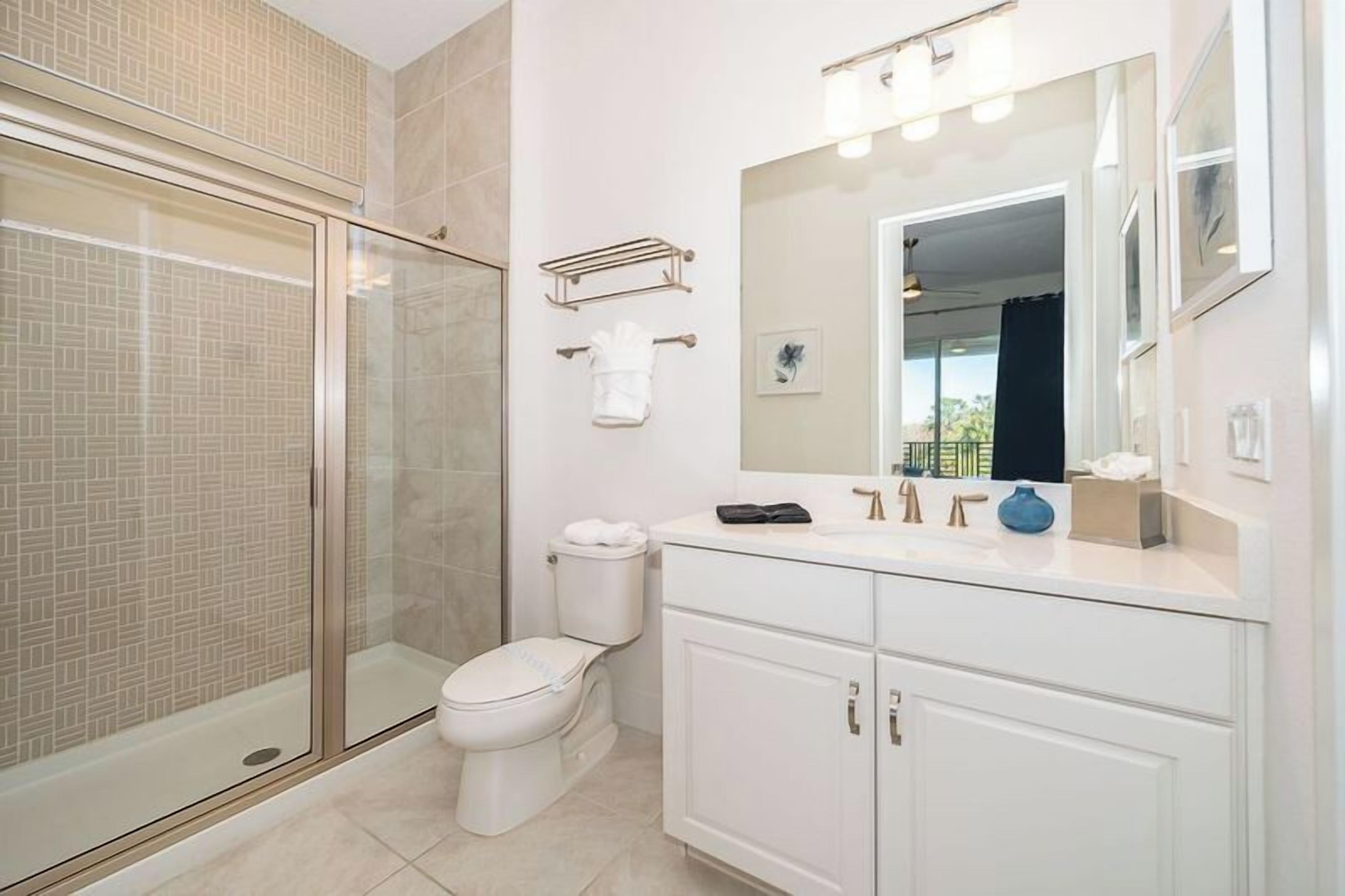 Un baño moderno con cabina de ducha de vidrio, inodoro, tocador con espejo y un ventanal pequeño.