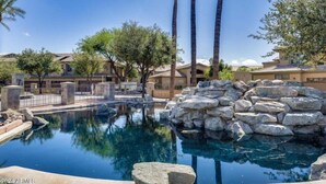 A swimming pool surrounded by rocks and palm trees, with buildings in the background. - The Bridges? How Fancy! Waterview, Garage, Pool. (Chandler)