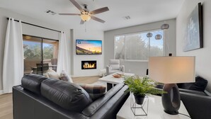 A modern living room with a black leather sofa, a white coffee table, a floor lamp, and a fireplace. - The Bridges? How Fancy! Waterview, Garage, Pool. (Chandler)