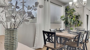 A dining area with a wooden table set for four, surrounded by chairs, a vase with branches, and a chandelier. - The Bridges? How Fancy! Waterview, Garage, Pool. (Chandler)