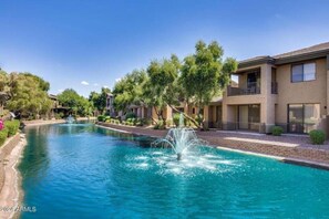 Uma piscina com fonte, cercada por árvores e um edifício com varandas.