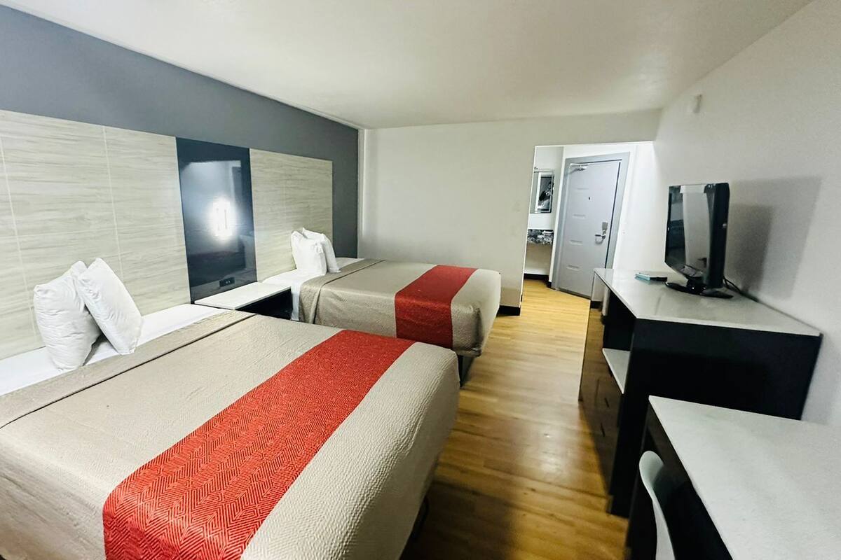 A hotel room with two beds, a desk, a television, and a mirror.