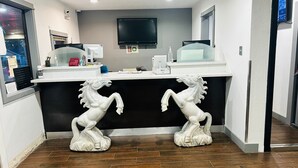 A reception area with a black counter, two white horse statues, a mounted TV, and a door with a number sign. - Evergreen Inn Portland Airport (Portland)