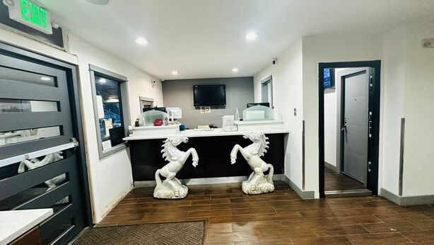 A hotel lobby with a reception desk, a mounted TV, and two white horse statues. - Evergreen Inn Portland Airport (Portland)