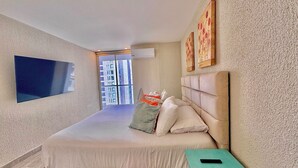 A modern bedroom with a large bed, a TV mounted on the wall, and a view of a building through the window.