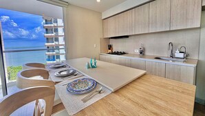 A modern kitchen with a large island, a view of the sea, and a dining area with a table set for four.