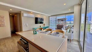 A modern kitchen with a large island, a dining area with chairs, and a view of the cityscape through large windows.