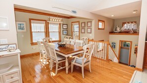 A dining area with a wooden table and white chairs, a staircase with a railing, and a shelf with model ships. - Oceanside,  Private Pool, Hot Tub, Community Amenities,  BH9, BeaContent (Corolla)
