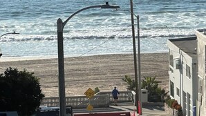 A beachside view with a street, a pedestrian crossing, and a building with a balcony.
