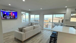 A modern living room with a large TV, a sofa, and a kitchen area with a bar.