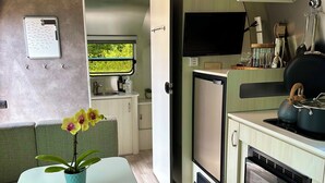 A compact kitchen with a microwave, stove, and sink. There's a small refrigerator and a flat-screen TV mounted above the counter.