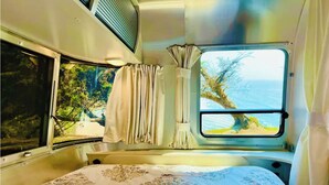 A cozy RV interior with a bed, curtains, and a window offering a scenic view.