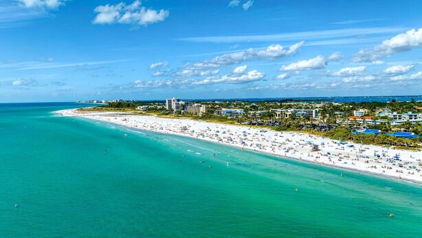 Ein Küstenstrand mit breitem Sandstrand, blauem Himmel und Gebäuden im Hintergrund.
