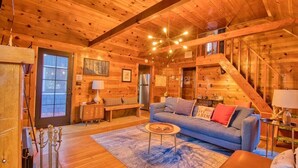 A cozy log cabin interior with a wooden staircase, a sofa, a coffee table, and a dining table.