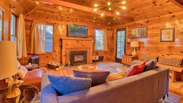 A cozy log cabin interior with a fireplace, wooden walls, a sofa, and a dining area.