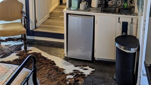A compact kitchen with a microwave, toaster, and small refrigerator. A chair and a cowhide rug are visible in the foreground. - The Half Pint - Pet Friendly for 1 Pet Only (Abilene)