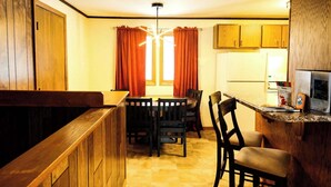 A compact kitchen with wooden cabinets, a dining table with chairs, and a refrigerator. - Winter Vacation Wonderland I Alpen Villas at Powderhorn Mountain (Bessemer Township)