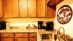 A kitchen with wooden cabinets, a granite countertop, a coffee maker, and a stainless steel sink. - Winter Vacation Wonderland I Alpen Villas at Powderhorn Mountain (Bessemer Township)