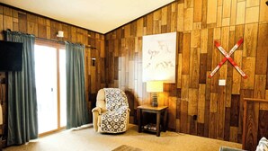 A living room with a wooden paneled wall, a beige armchair, a small table with a lamp, and a television on the left. - Winter Vacation Wonderland I Alpen Villas at Powderhorn Mountain (Bessemer Township)