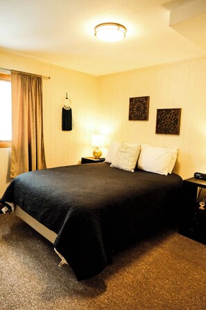 A hotel room with a large bed, a bedside table with a lamp, and a window with curtains.