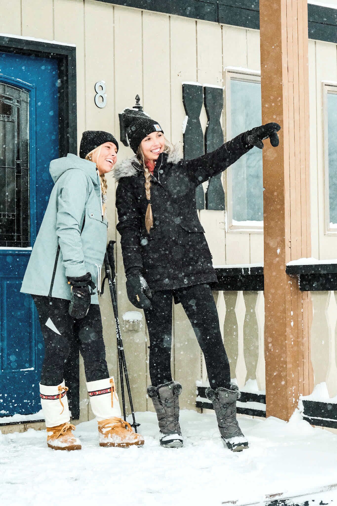 Dos personas con ropa de invierno frente a una casa con puerta azul y el número 8 en la pared.