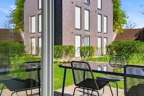 Un patio con una mesa y sillas de vidrio, un edificio de ladrillo al fondo y un césped bien cuidado.