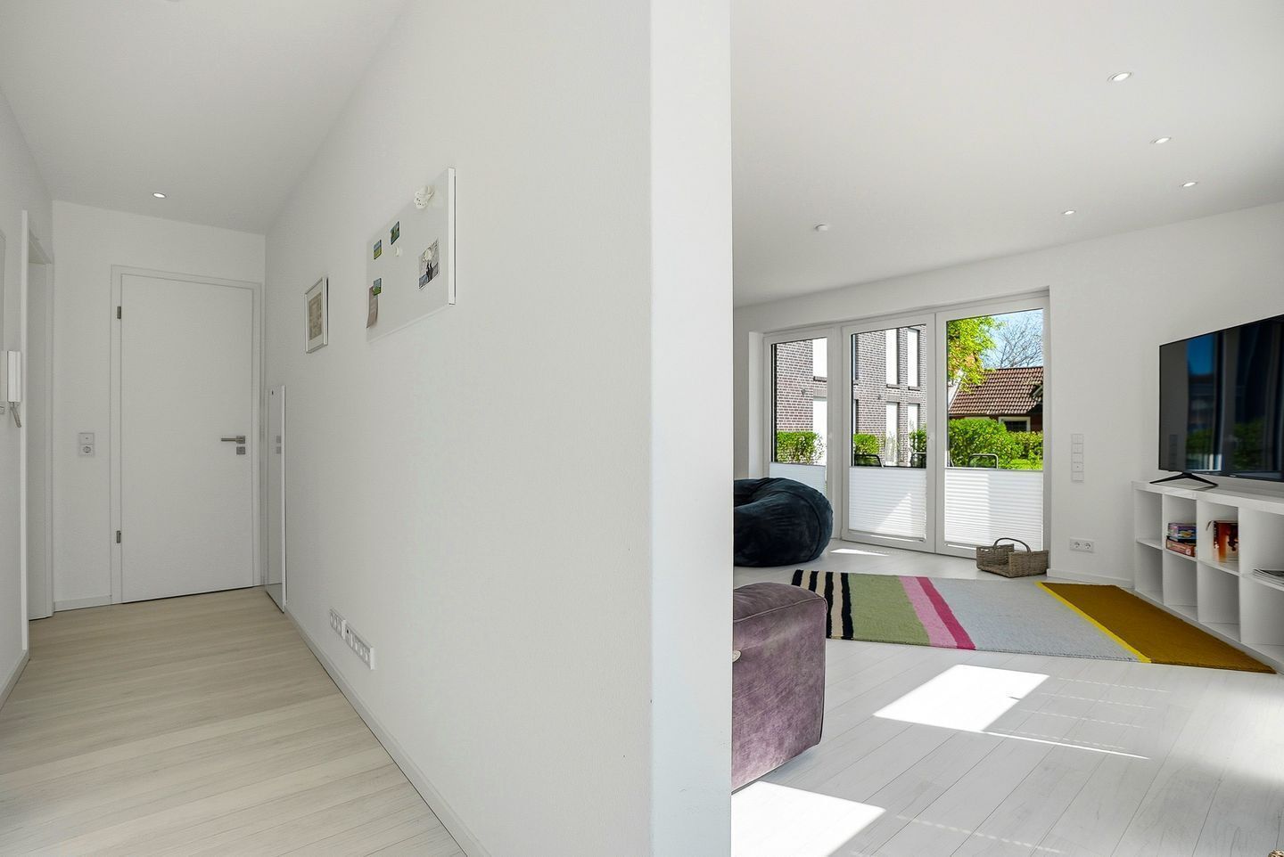Ein modernes Interieur mit einem Flur, der in einen Wohnbereich mit großem Fenster, Fernseher und Sitzsack führt.