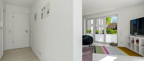 Ein modernes Interieur mit einem Flur, der in einen Wohnbereich mit großem Fenster, Fernseher und Sitzsack führt.