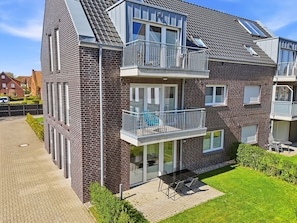 A multi-story residential building with a brick facade, balconies, and a patio area with outdoor furniture. - Glücksinsel Norddeich - 70sqm vacation apartment for up to 2 persons with garden and (Norddeich)