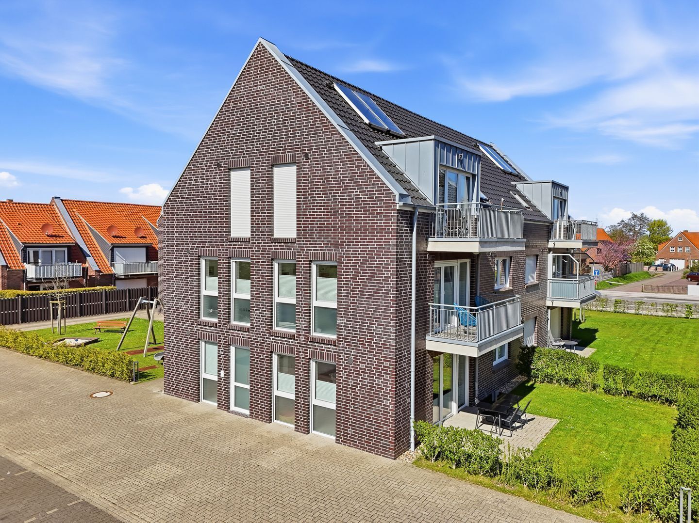 Un immeuble résidentiel moderne à deux étages, doté d’une façade en briques, de grandes fenêtres et d’un balcon.