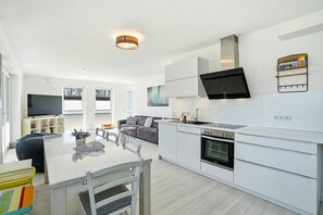 Una cocina moderna con armarios blancos, horno integrado y televisor de pantalla plana.