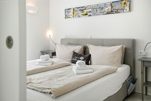 Una habitación de hotel moderna con una cama, dos almohadas, una mesita de noche, una obra de arte en la pared y un mueble auxiliar.