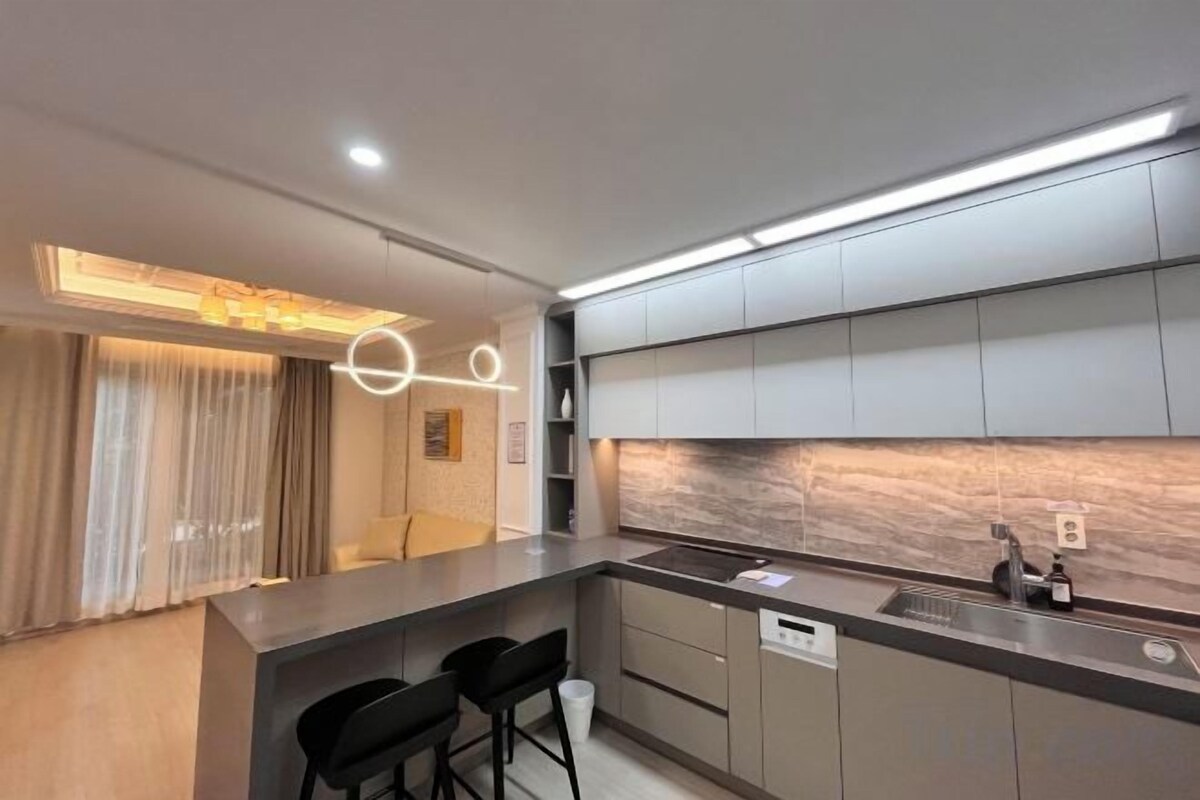 A modern kitchen with a marble backsplash, recessed lighting, and a bar area with stools.
