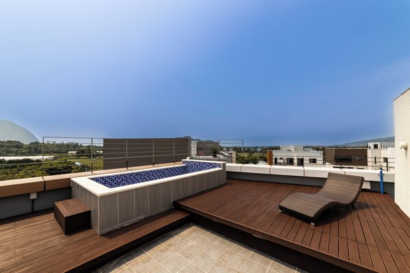 A rooftop terrace with a swimming pool, wooden deck, and a lounge chair.