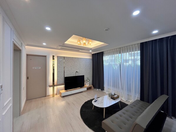 A modern living room with a flat-screen TV, a sofa, a coffee table, and a large window with curtains. - Hermen House in Jeju (Seogwipo)