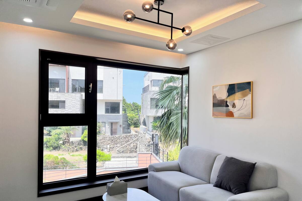 A modern living room with a large window, a sofa, a coffee table, and a painting on the wall.