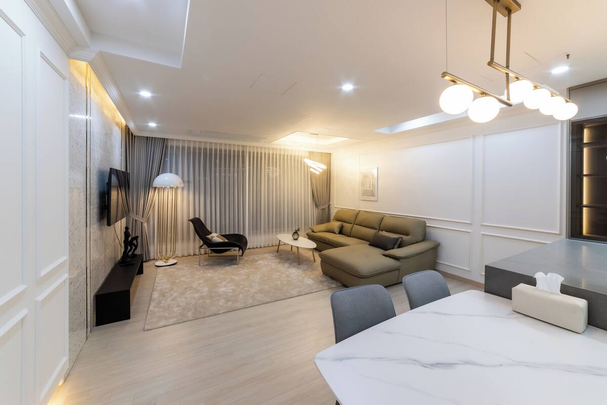 A modern living room with a sofa, a dining table, and a TV mounted on the wall.