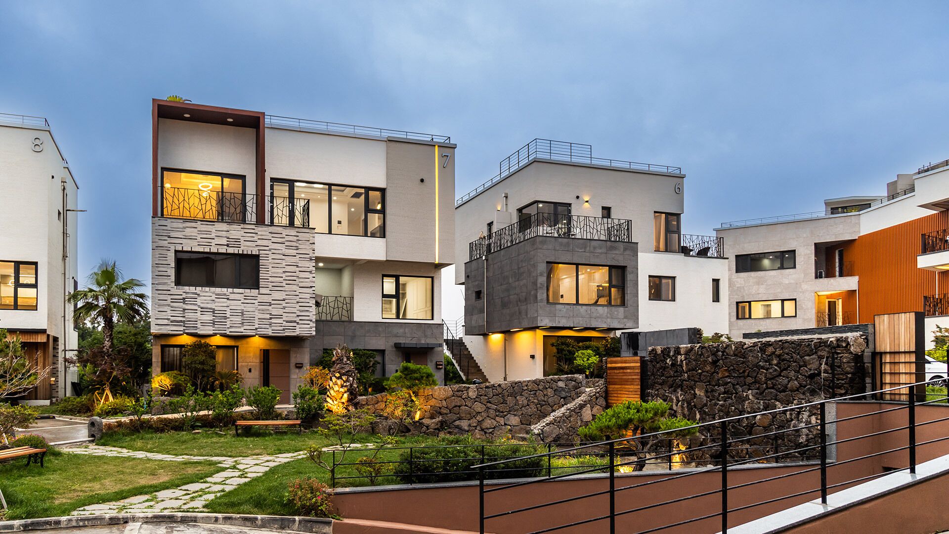 A modern multi-story residential building with a stone facade, multiple balconies, and a landscaped garden.