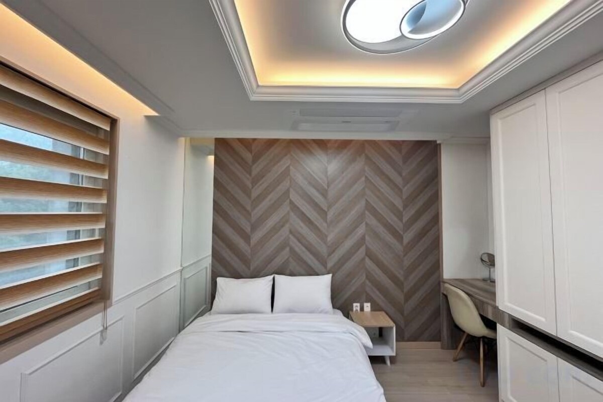 A modern bedroom with a bed, bedside table, and a herringbone-patterned wall.