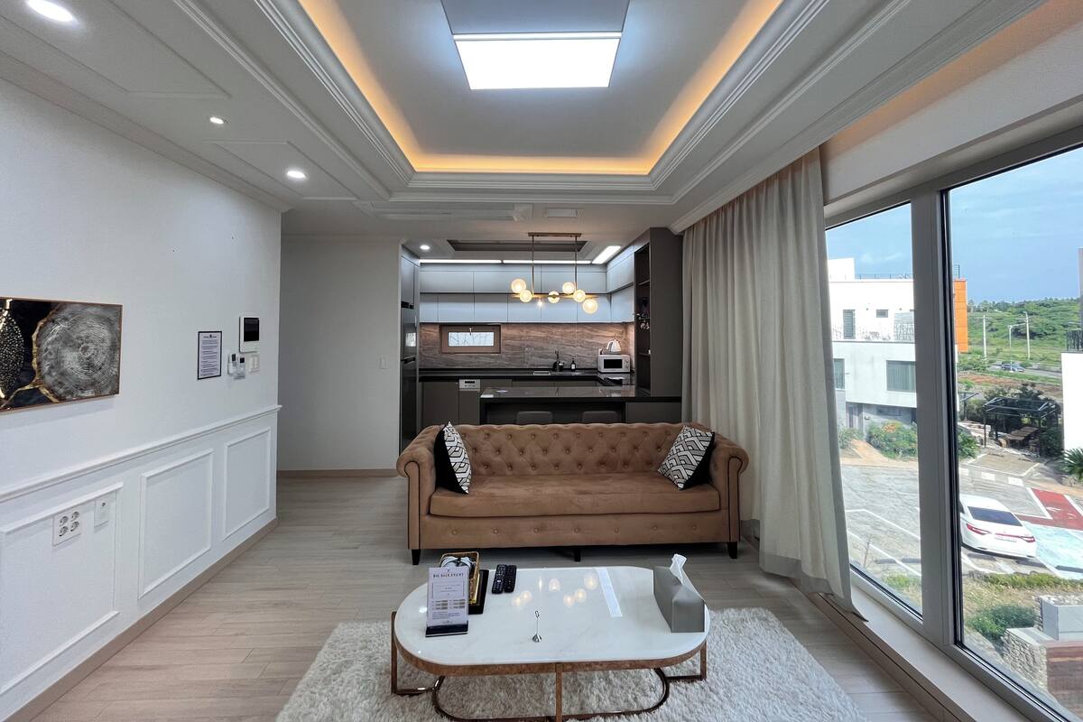 A modern living room with a sofa, coffee table, and a view of the city through large windows.