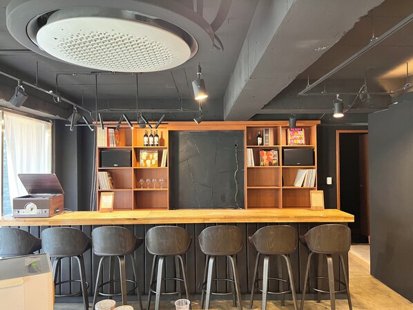 A bar area with a wooden counter, black bar stools, and shelves with books and bottles. - Hermen House in Jeju (Seogwipo)